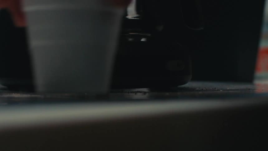 Persons hand turning on a coffee maker and picking up a disposable cup