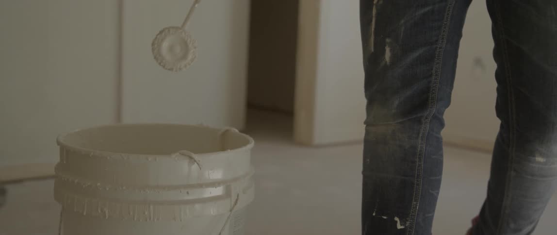 A person dips a paint roller in a bucket