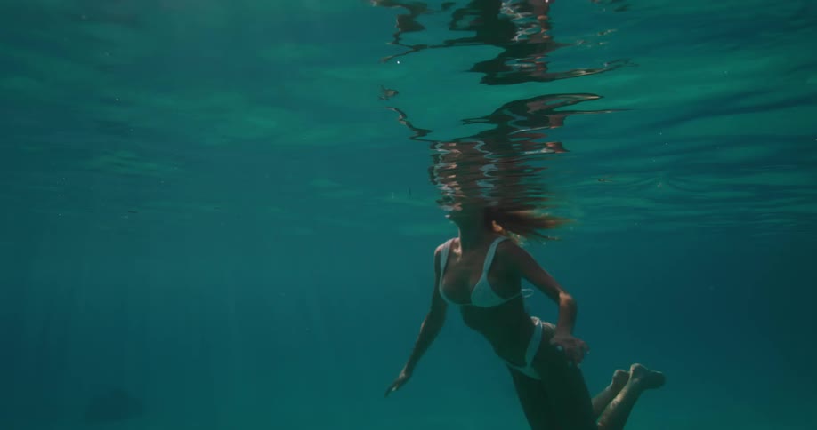 Woman swimming in a vast blue ocean wearing a white bikini