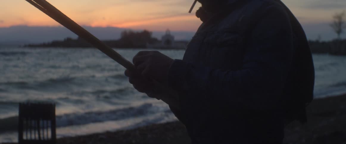 A man smokes and fiddles with something on the beach