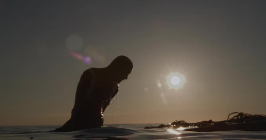 Silhouette of a woman in a bikini emerging from the ocean waters against the sun on the horizon