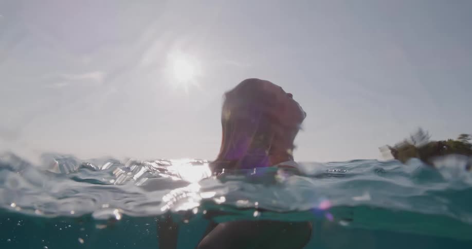 A woman in a white bikini is swimming underwater and releasing several bubbles with her mouth