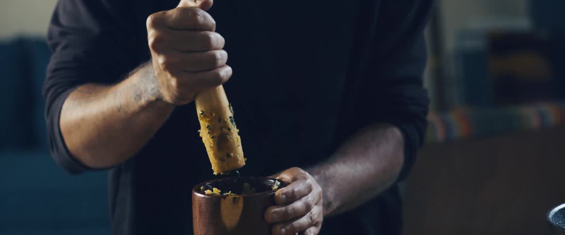 Closeup of a mans hands squeezing a fruit into a wooden bowl