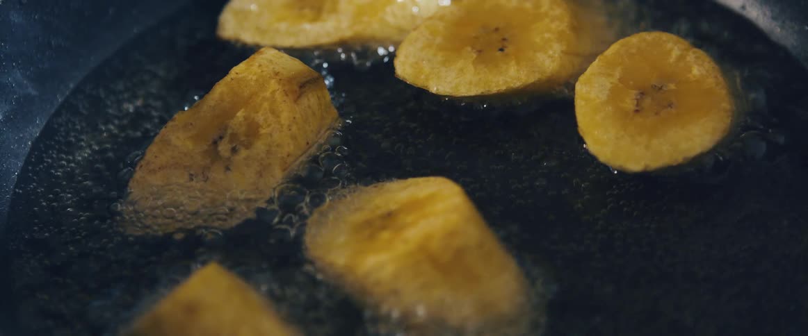 Closeup of a frying pan with sliced plantains being fried