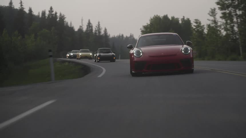 Sports cars of different colors driving on a road with trees around