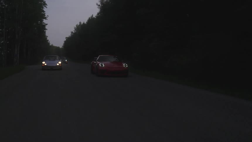 New Porsche passing classic Porsche on a road with trees around at dusk