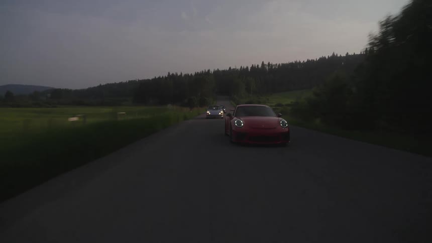 Red Porsche sports car driving on a rural road