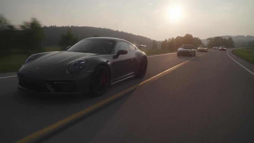 A black sports car driving on an asphalt street and there are some cars behind it