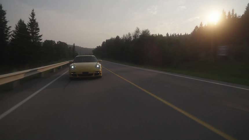 A yellow sports car driving on an asphalt street and behind it is another sports car