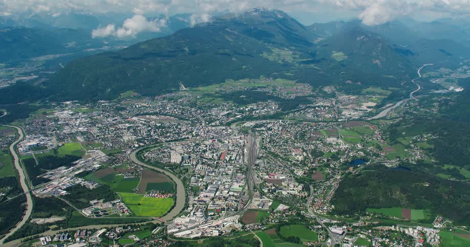 Roads and rivers wind through a large town in valley near forested mountains on a foggy day