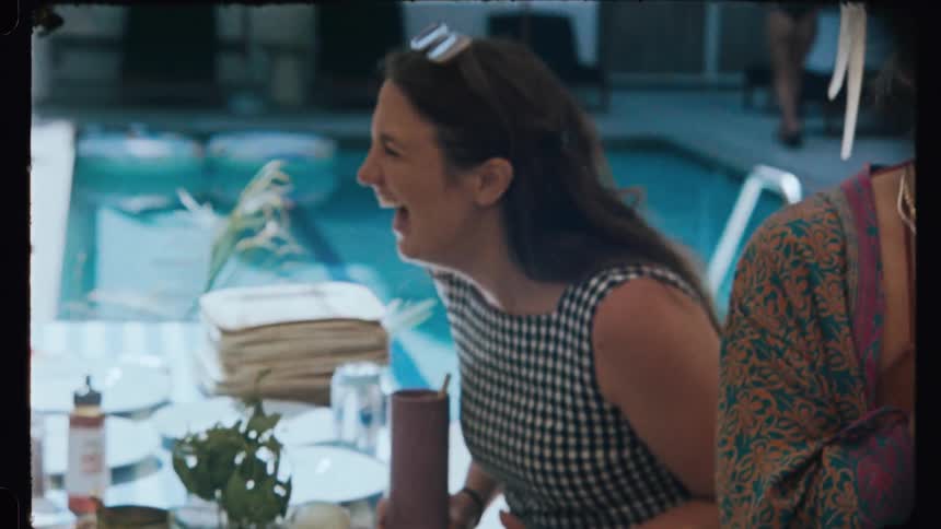 Woman sitting at a table surrounded by people next to the pool laughing