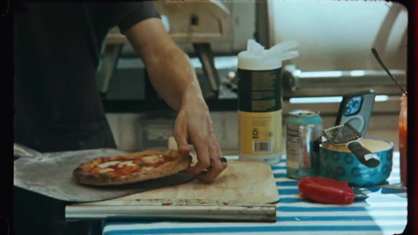 A person is placing a small pizza that is on a wooden cutting board into a tool to go into the oven