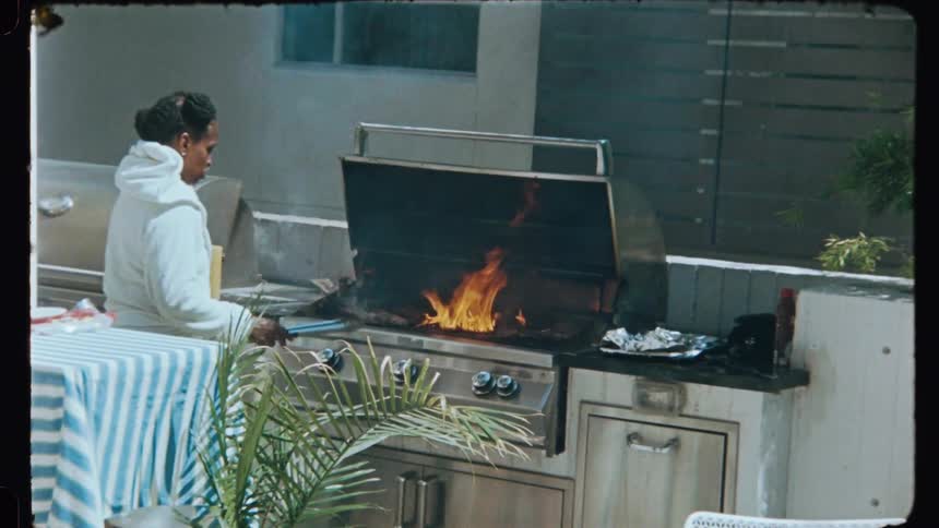People at a party with one of them roasting meat on a barbecue grill