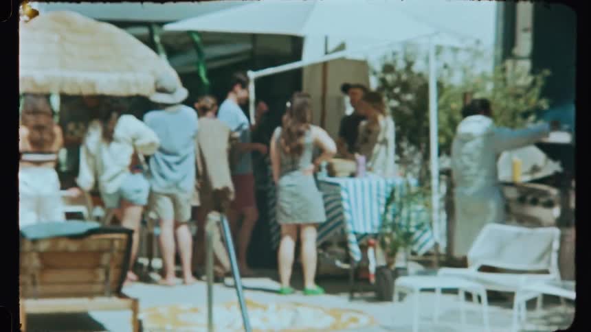 Several people gathered behind a house having a barbecue near the pool