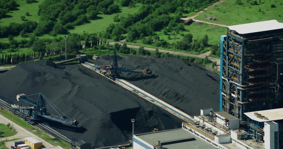 This aerial view shows a coal fired power plant with smokestacks cooling towers and coal storage silos surrounded by trees