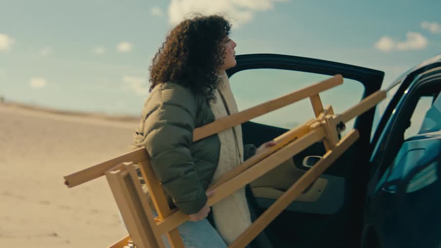 Curlyhaired woman taking an artistic fourshot from the backseat of a blue sedan vehicle