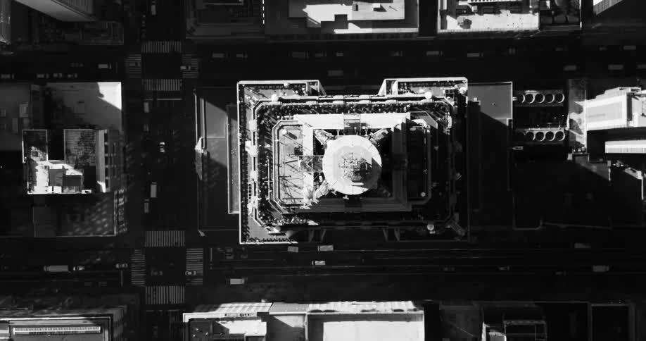 An aerial view of a large building in a metropolitan city seen from above in black and white tones