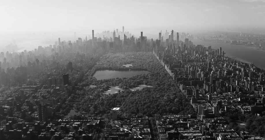 An aerial view of central park surrounded by several tall metropolitan buildings in black and white tones