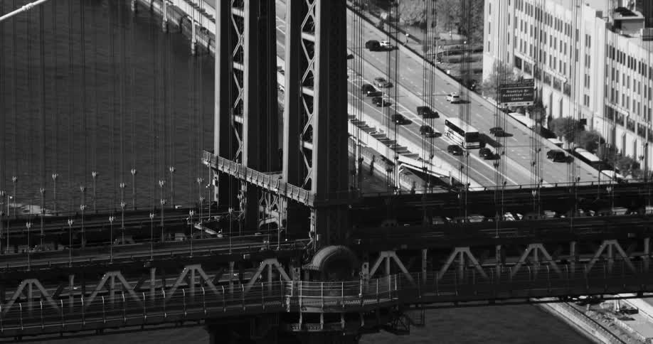 An aerial black and white footage of a suspension bridge near the city