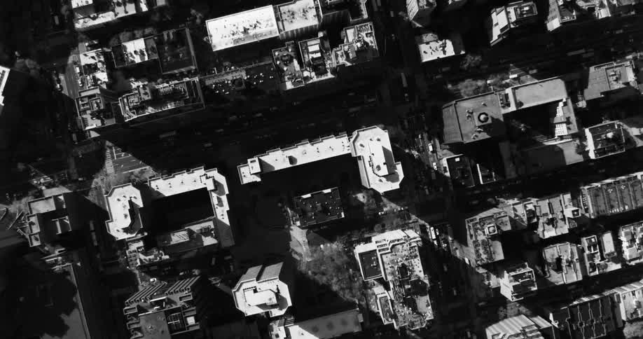 An aerial view of a metropolitan city with diverse buildings and houses and wide streets in black and white tones