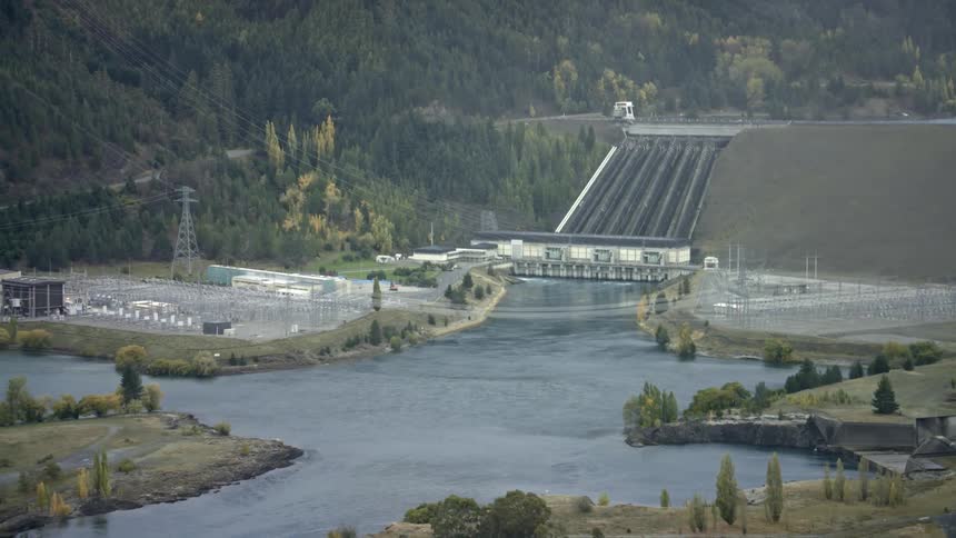 Power lines cross river and run up forested mountain slope near hydroelectric dam