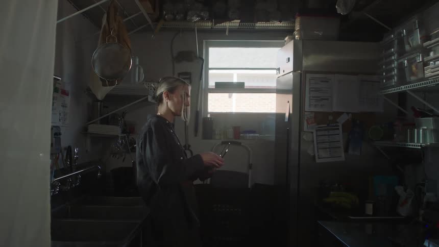 Woman indoors working in the kitchen putting on headphones