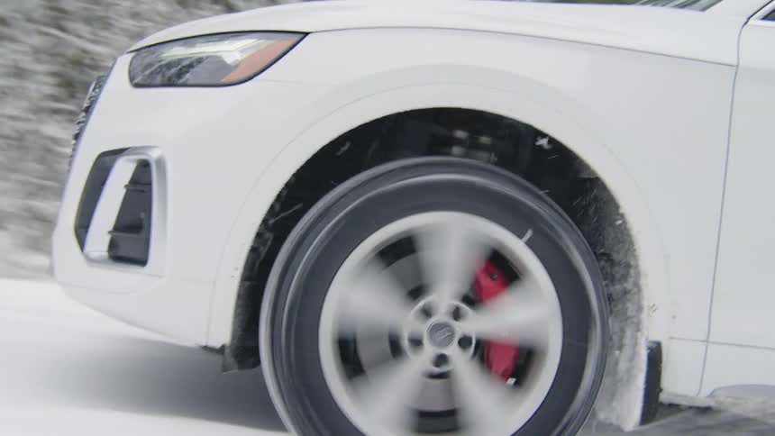 Wheel of an uphill car accelerating on a snowy track with conifers on the side