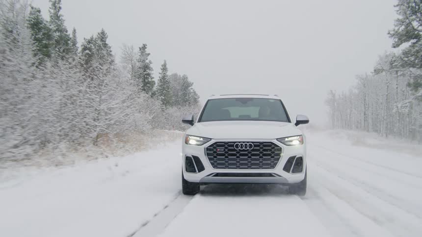 White audi speeding on a snowcovered road with conifers around