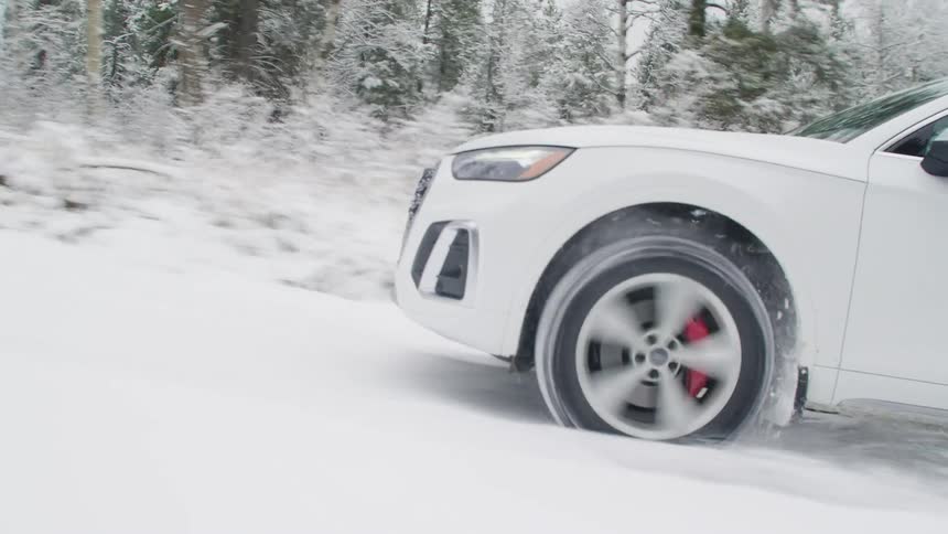 Man drives white car up snow covered slope past ice frostedforest