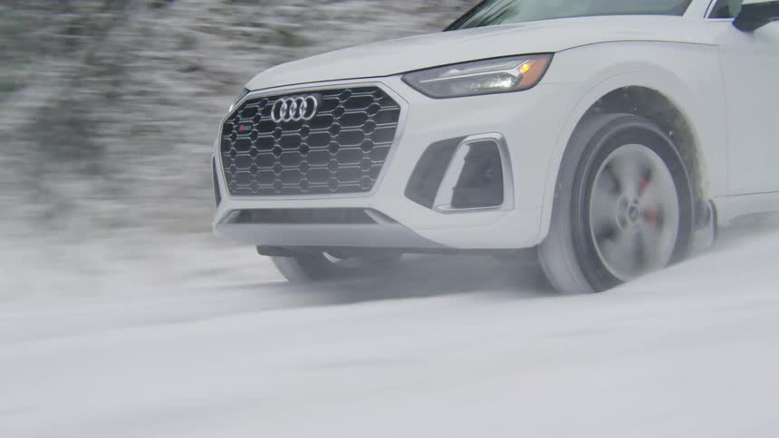 A white audi driving down a snow covered road through a forest