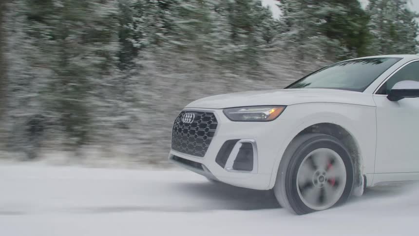 A white audi drives over a snow covered road