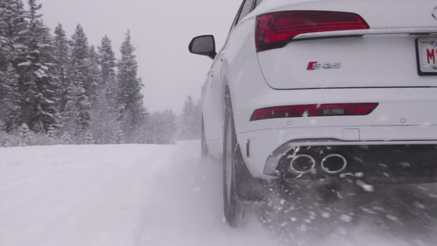 A white car driving on a road covered in white snow