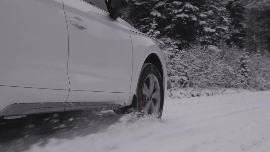 A closeup of a white cars driving through snowcovered ground near a forest