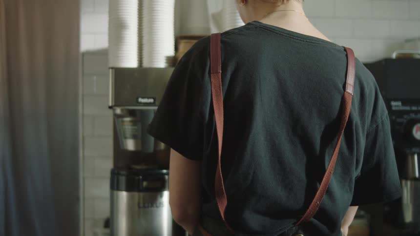 A blonde cashier is talking to someone in front of her with a smile on her face and she takes the order on the computer and then gets a coffee in a cup