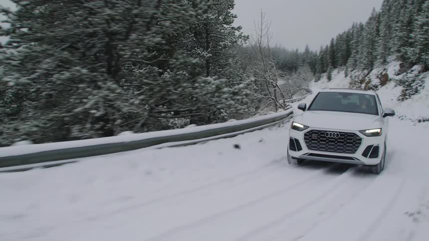 White audi suv traveling along a snowcovered road with conifers around