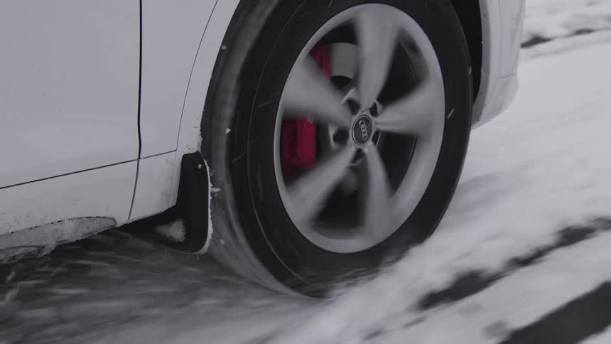 A closeup of the front wheel of a white car driving on a snowcovered road