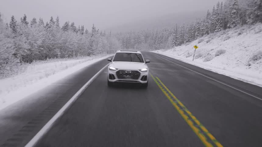 A white car drives down a country road in the winter