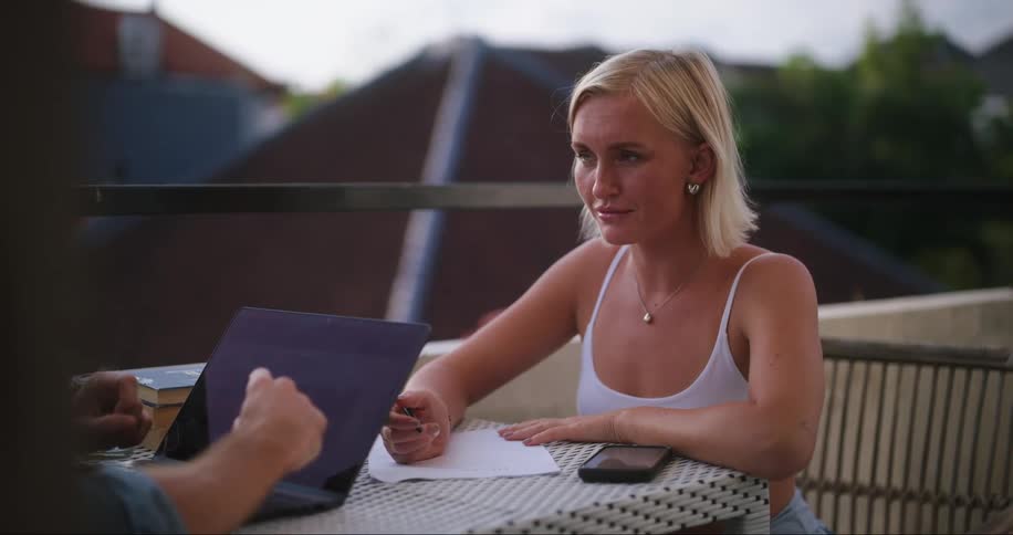 Two people sitting at a table with laptop and smartphone talking