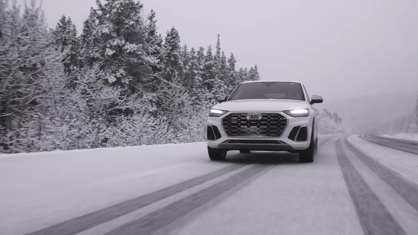 A white vehicle drives on a snowy road by a forest