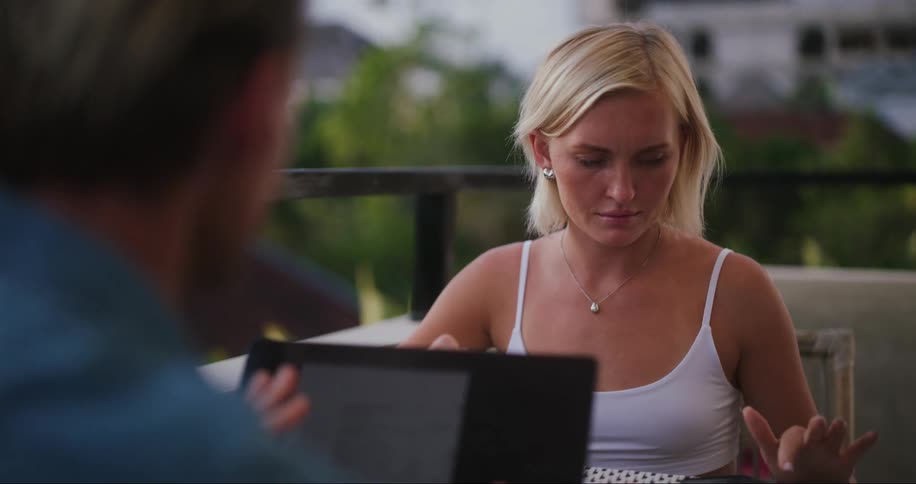 A man and a woman talk while using a laptop and smartphone