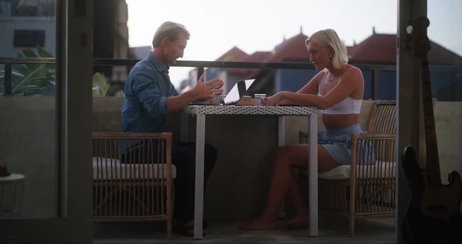A man and a woman sit outside on a balcony
