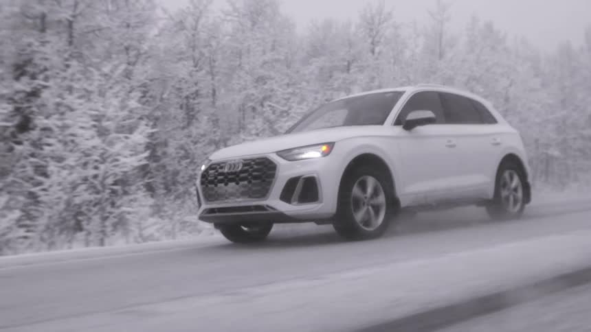 A white vehicle drives on a slick road next to a forest