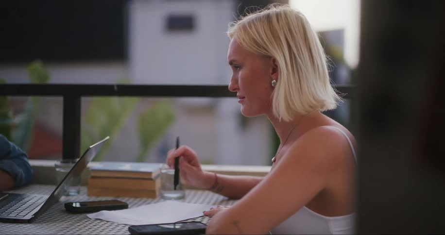 Two people sitting on the balcony with a laptop on cell phones talking face to face