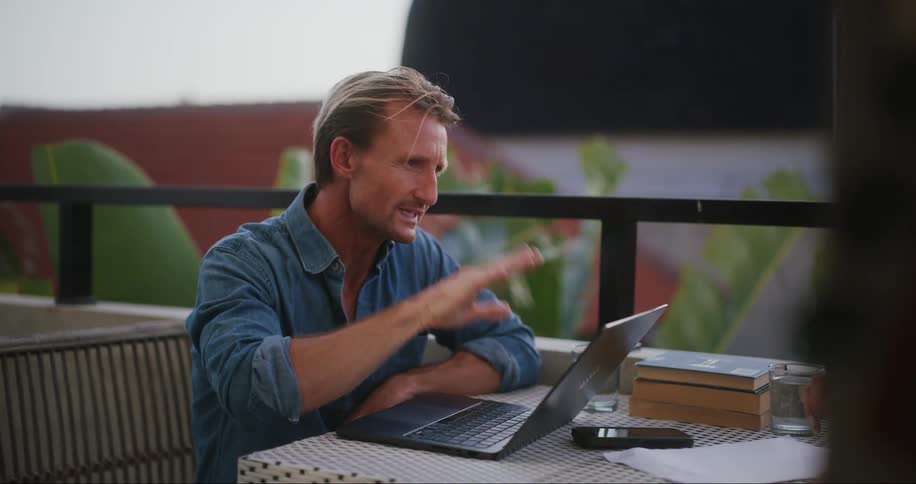 Man sitting at a table with laptop in front of him open and talking