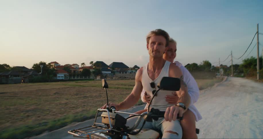 A woman holds on to a man driving a motorcycle over a dirt road