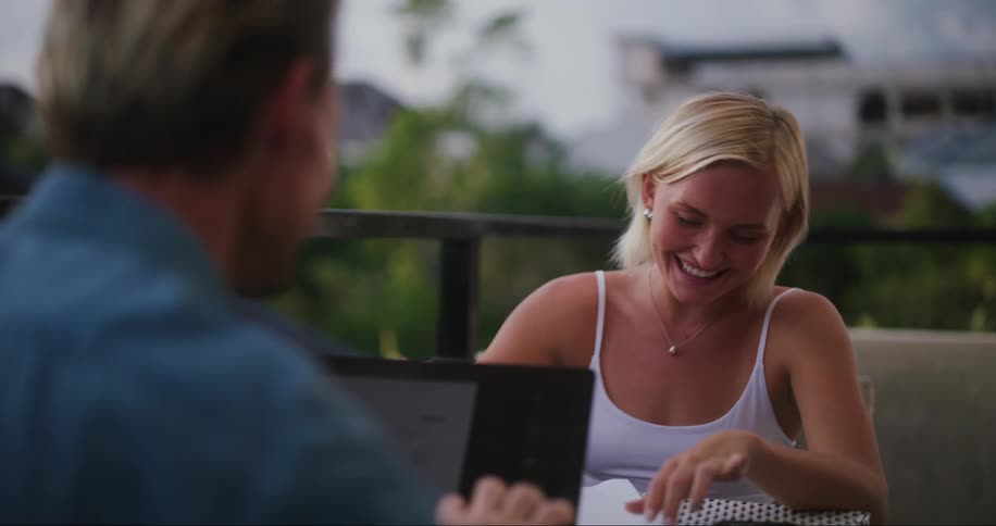 Blonde woman sits at a table with man highfives and laughs