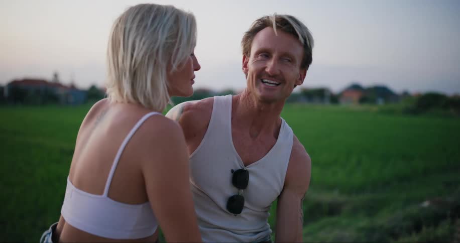 A young couple sitting in a field talking to each other at evening