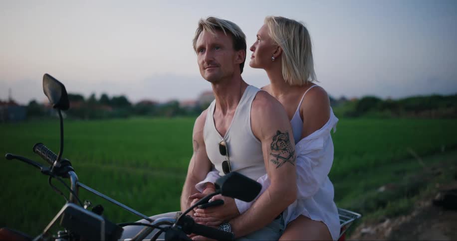 Man and woman sit on motorcycle outdoors near green field