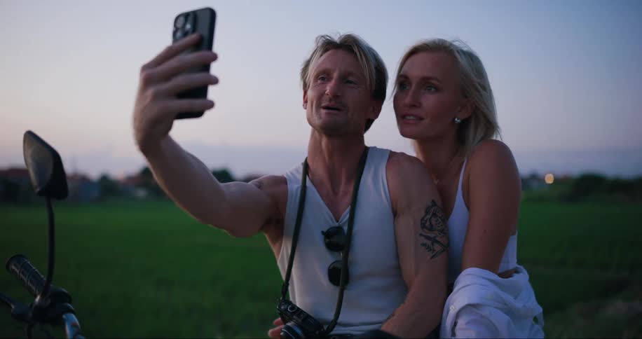 A man and a woman are taking a selfie with a cell phone held by a man who is smiling