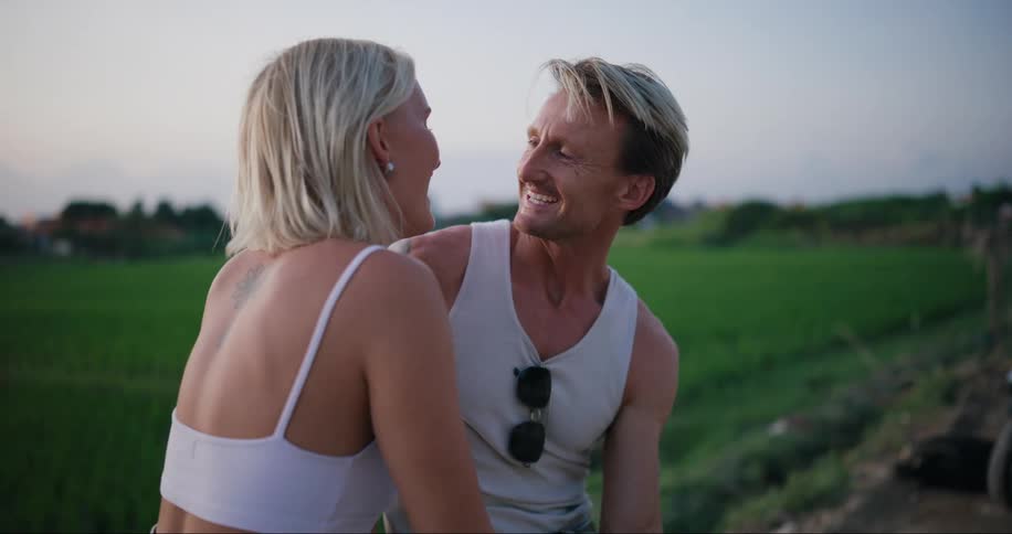Smiling oneman and onewoman couple kissing while standing on the edge of a farm field